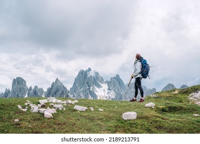 Woman trekker with backpack and trekking poles on the hill enjoying picturesque Dolomite Alps view near Tre Cime di Lavaredo formation in South Tyrol, Italy. Active people and mountain concept. 