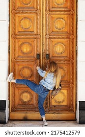 A woman tries to forcefully open massive wooden doors with a classic pattern. Break into a locked door.