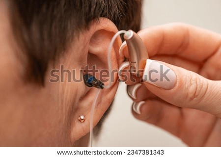 A woman tries on a hearing aid hidden in her ear on a light background. Restoration of hearing. Technical means