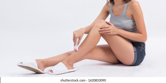 Woman trimming her leg with electric trimmer on white background