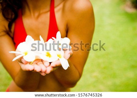 Woman in a tropical setting holding frangipani.