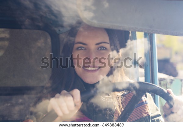 woman truck driver in the car. Girl\
smiling at camera and holding the steering\
wheel