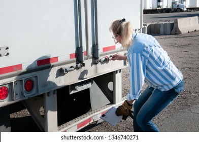 Woman Truck Driver Checking Her Trailer Seal Number To Make Sure It Matches The Numbers On Her Bill Of Lading.