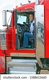 Woman Truck Driver Looking Out The Door Of A Big Rig From The Driver's Seat