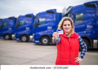 Woman truck driver proudly holding commercial driving license. In background parked trucks. Truck driving school and job openings for new drivers.