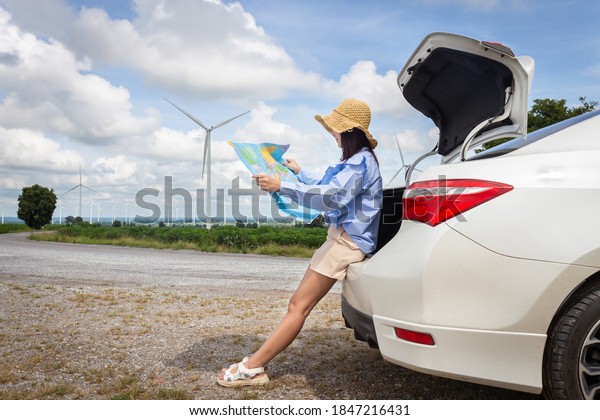 woman in the trunk of a car looking at a map\
to reach the holiday destination with blue sky and wind turbines\
background