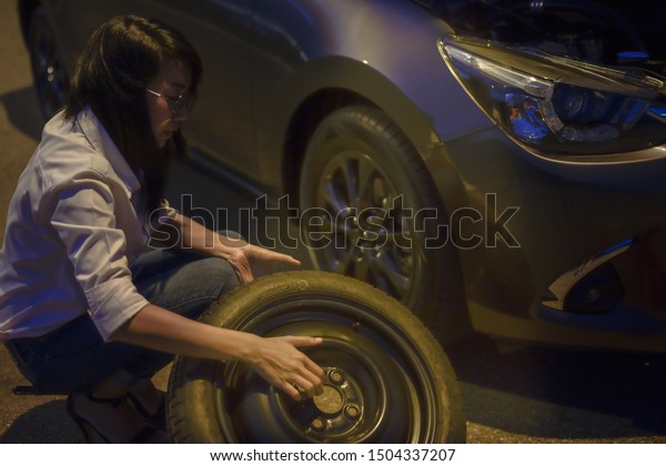 Woman try to fix problem of car by herself
with belonging tools, need help and assistant at dark of the night,
scary and worry alone in the dark, car engine failure or tire need
replacement