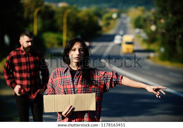 Woman try to stop car with blank cardboard sign and\
gesture. Couple in love travelling by hitchhiking, copy space.\
Travelling and hitchhiking concept. Couple with pensive faces\
travel by auto stop.