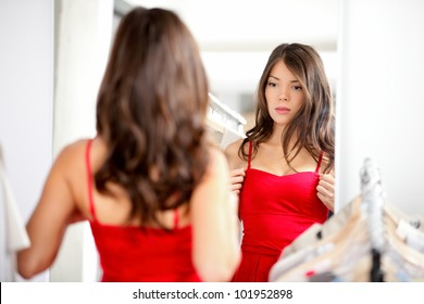 Woman trying clothing looking in mirror adjusting dress. Beautiful young multiethnic girl.