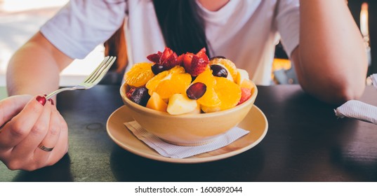 Woman Trying Exotic Dish In Street Cafe. Adult Lady Taking Piece Of Fruit From Plate And Chewing Food While Resting In Street Restaurant.