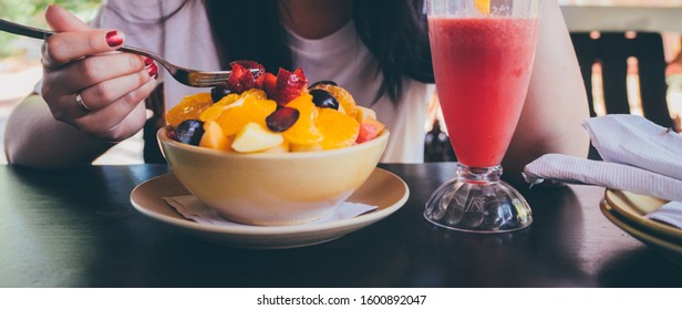 Woman Trying Exotic Dish In Street Cafe. Adult Lady Taking Piece Of Fruit From Plate And Chewing Food While Resting In Street Restaurant.