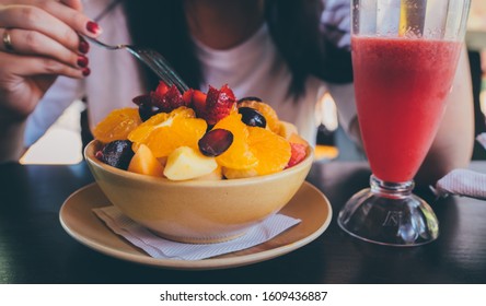 Woman Trying Exotic Dish In Street Cafe. Adult Lady Taking Piece Of Fruit From Plate And Chewing Food While Resting In Street Restaurant.