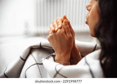 Woman is trying to keep warm, rubbing her hand in hand, she blows warm air from her mouth on her hands. High taxes make it impossible to heat the apartment in full mode. Behind the woman is a battery - Powered by Shutterstock