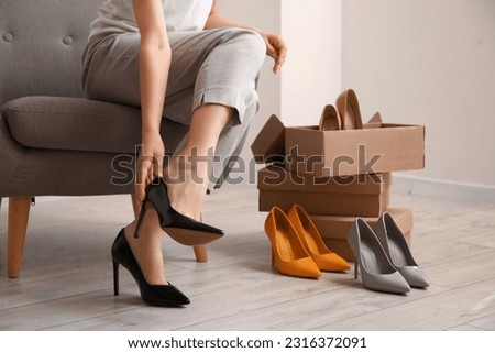 Woman trying on stylish high heeled shoes in room
