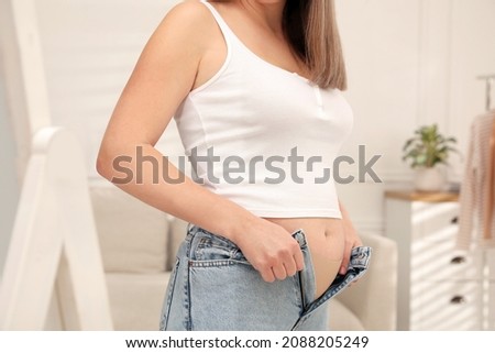 Woman trying to put on tight jeans at home, closeup