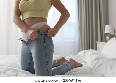 Woman trying to squeeze into tight jeans on bed at home, closeup