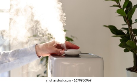 Woman turn on and inhaling aroma oil steam from humidifier. Humidification of air in the apartment during the period of self-isolation due to coronavirus pandemic