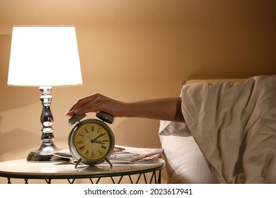 Woman Turning Off Alarm Clock In Bedroom At Night