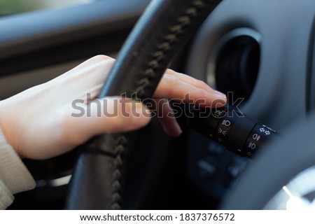 Woman turning on left signal switch, close up shot of her hand. Car interior details. 