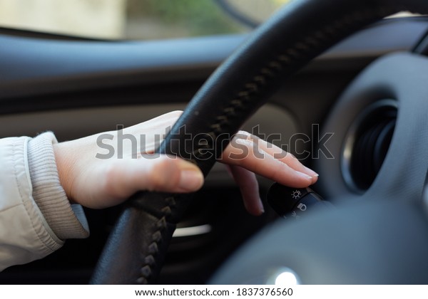 Woman turning on left signal switch,\
close up shot of her hand. Car interior details.\
