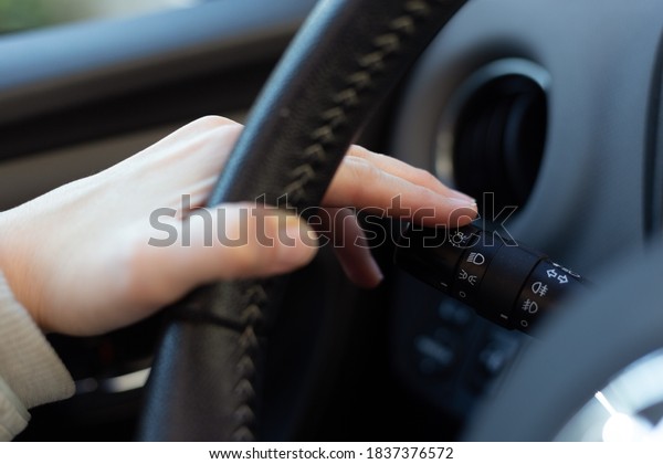 Woman turning on left signal switch,\
close up shot of her hand. Car interior details.\
