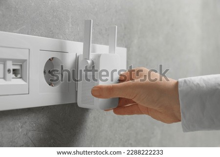 Woman turning on wireless Wi-Fi repeater indoors, closeup
