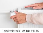 A woman turns up the temperature on a heating radiator as the cold weather sets in, adjusting to the changing seasons, seeking warmth and comfort at home, needing for increased heating during cold