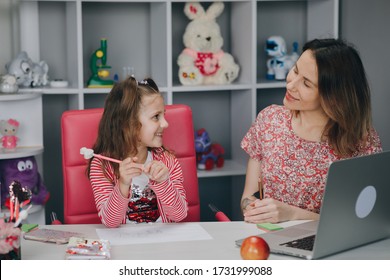 Woman Tutor Or Foster Parent Mum Helping Cute Caucasian School Child Girl Doing Homework Sitting At Kitchen Table. Diverse Nanny And Kid Learning Writing In Notebook Studying At Home.