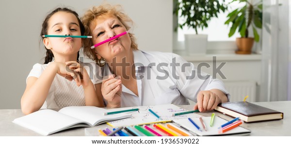 Woman tutor or\
foster parent mum helping cute caucasian school child girl doing\
homework sitting at table. Diverse nanny and kid learning writing\
in notebook studying at\
home.