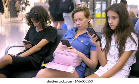 A woman and two Children in the airport waiting area use a smartphone. travel concept