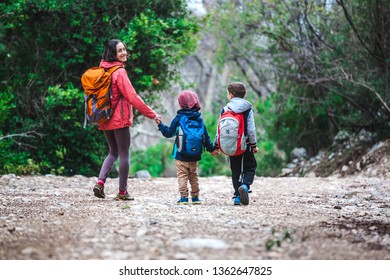 A woman with two children goes through the forest. The boy walks in the park with his mother and brother. Family holiday. Brunette with a backpack travels with children. Mom holds sons hands. - Shutterstock ID 1362647825