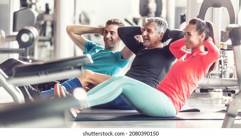 A Woman And Two Men Of Different Generations Work Out Together In The Gym Doing Coordinate Situps.