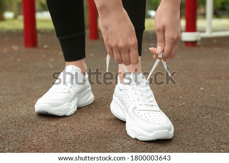 Woman tying laces of stylish sneakers outdoors, closeup