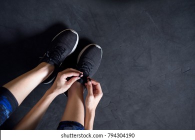 Woman Tying Running Shoes On Black Floor Background In Gym.