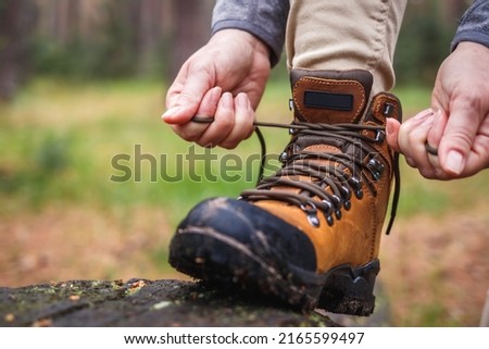 Woman tying shoelace on her hiking boot. Tourist is getting ready for hike at forest trekking trail