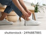 Woman tying shoelace of white sneaker indoors, closeup