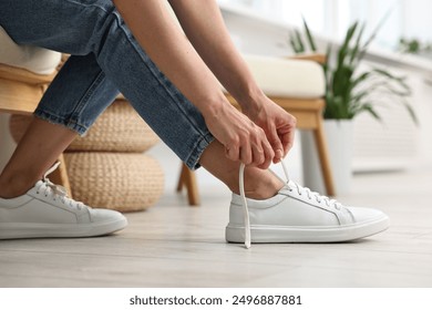 Woman tying shoelace of white sneaker indoors, closeup - Powered by Shutterstock