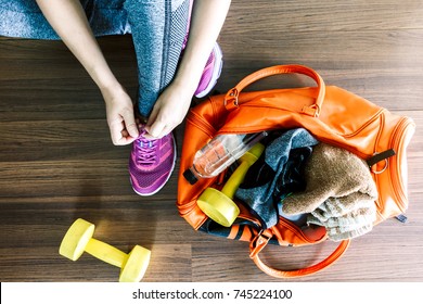 Woman tying shoelaces with bag and fitness equipment