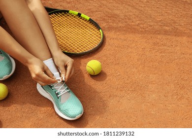 Woman tying shoelaces on clay court with racket and tennis balls - Powered by Shutterstock