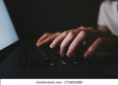 Woman Is Typing On A Laptop Keyboard While Lying On A Sofa At Home In The Dark. White Laptop Screen