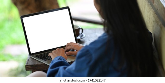 Woman Typing On White Blank Screen Computer Laptop That Putting On Wooden Working Desk While Sitting Outside The House Over Nature As Background.