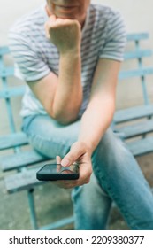 Woman Typing Text Message On Mobile Smart Phone While Sitting On Wooden Bench. Female Person Wearing Jeans Trousers And Stripped T-shirt Using Smartphone For Communication. Selective Focus.