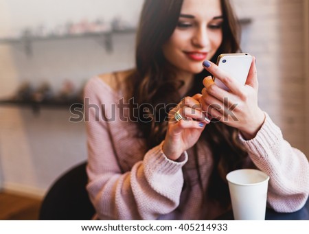 Woman typing write  message on smart phone in a  modern cafe. Cropped image of young  pretty girl sitting at a table with  coffee or cappuccino  using mobile phone.
