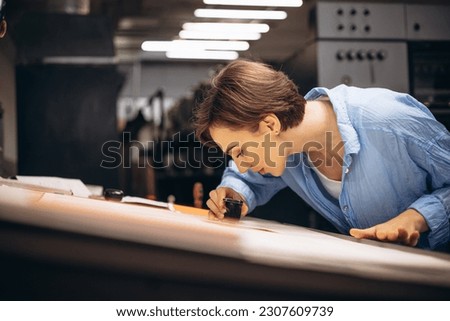 Woman typographer working in printing house with paper and magnifying lens