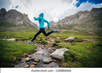 Woman Ultra Marathon Trail Runner Jumping Over Small River On Beautiful Mountains