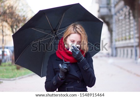 Woman with umbrella and a handkerchief. fall sick girl blows her nose in a handkerchief. Seasonal colds on a rainy day. Sad blonde sneezes, outdoors or outside
