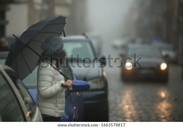 A woman\
with an umbrella on a foggy city\
street.