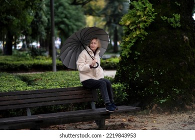 A Woman With An Umbrella Sits On A Park Bench In Rainy Weather.