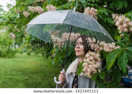 Woman under an umbrella in the rain near a chestnut tree.
