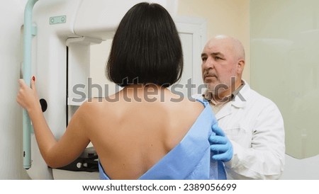 A woman undergoes a mammogram in a modern clinic under the supervision of a male doctor. A doctor installs a digital mammograph for a patient. Women's health concept.
